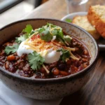 Bowl of beef brisket chili garnished with sour cream, cheese, and cilantro, served with cornbread.